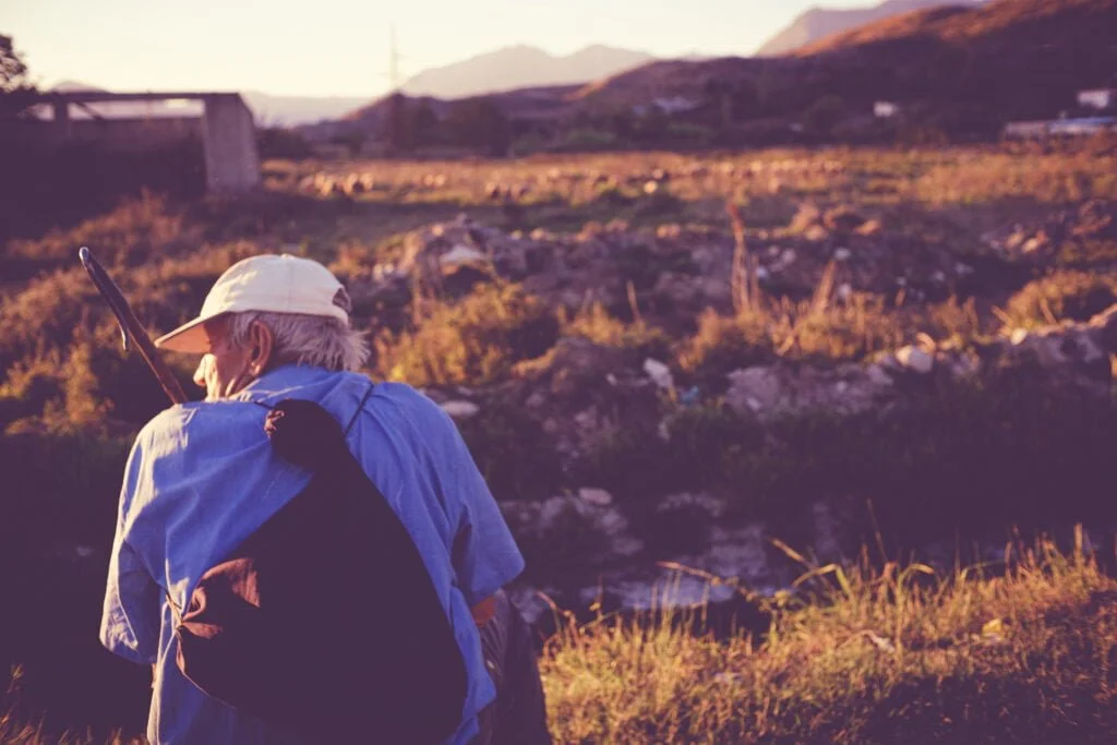 Elderly man contemplating the horizon in a countryside, embodying nomad journalism and slow traveling.