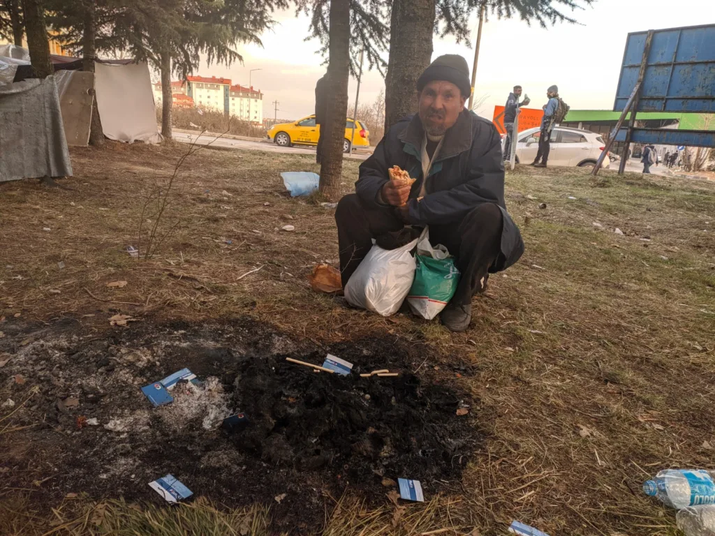 Man squatting in front of ashes of his belongings